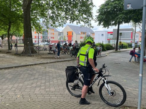 Ein Polizeibeamter auf einem Fahrrad steht vor einer Schule