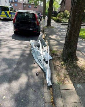 Teile der abgerissenen Markise liegen auf der Straße am rechten Seitenrand. Davor steht ein unbeteiligtes dunkles Fahrzeug, während ein Streifenwagen etwas weiter entfernt und auf der anderen Straßenseite steht.