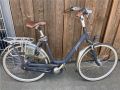 ein Fahrrad mit tiefem Einstieg und LEdersattel steht mit dem Lenker angelehnt an einer Holzfassade